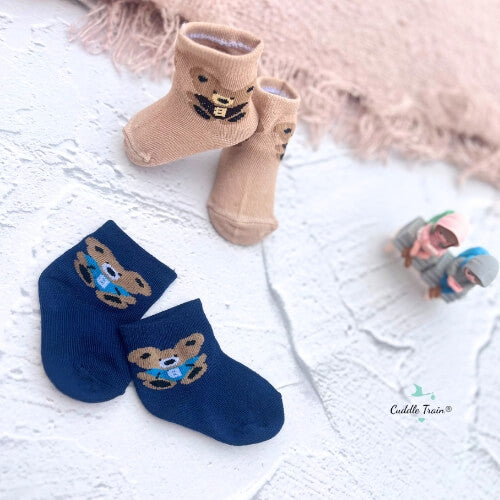 Pair of beige and blue socks with teddy bear design on a light wooden surface.
