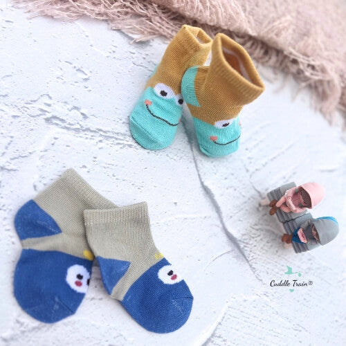 Pair of blue socks with cartoon face design on a white surface, brand 'Cuddle Train' visible.