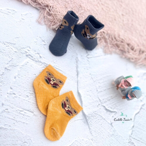 Pair of blue socks with teddy bear design on a textured white surface.