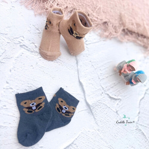 Two pairs of socks with bear designs on a textured surface, with a small toy in the background.