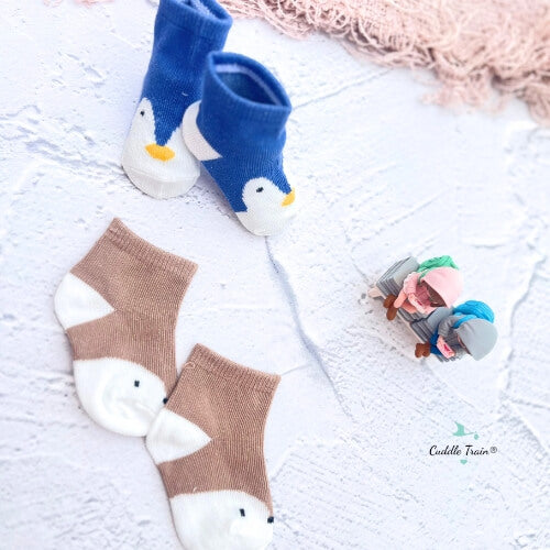 Pair of penguin-themed socks on a light wooden surface with a small bottle of lotion.