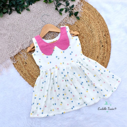 White dress with colorful polka dots and pink collar on a hanger against a textured surface.