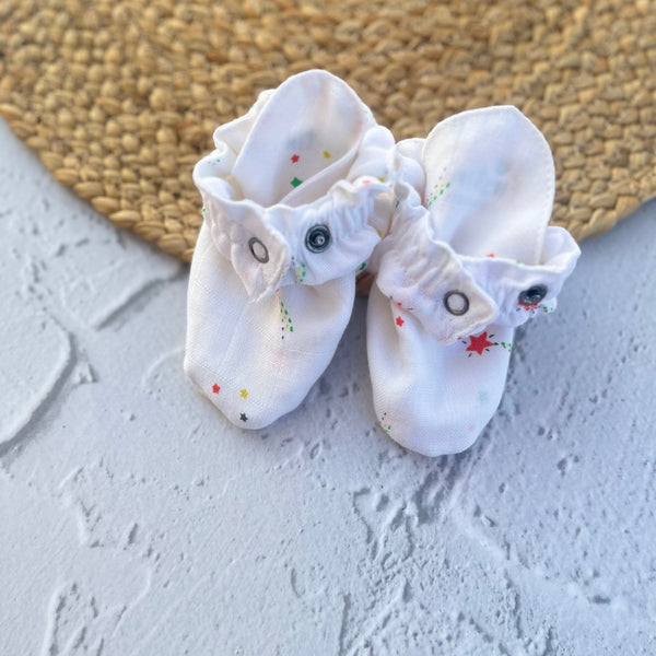 Pair of white baby socks with decorative elements on a textured surface.