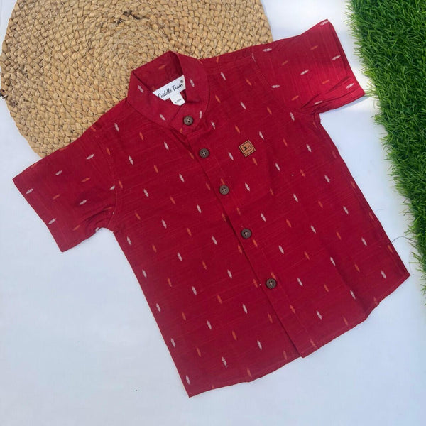 Red patterned shirt on a white surface with a woven mat and grass in the background
