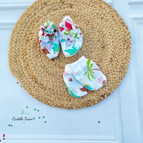 Two pairs of baby shoes with floral and animal designs on a woven mat.
