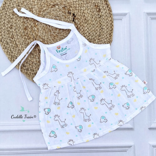 White baby dress with animal pattern on a white surface with a straw hat.