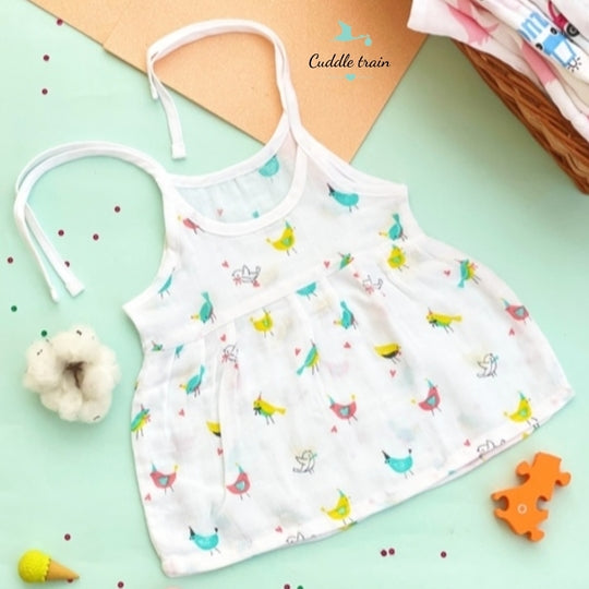 Children's white tank top with colorful bird pattern on a light green surface.
