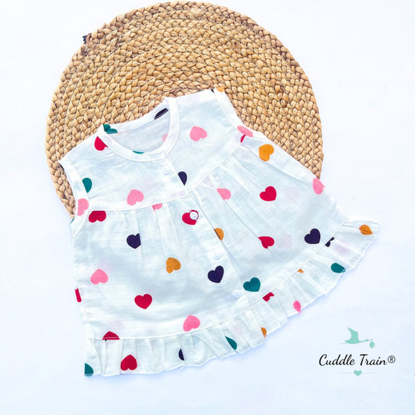 White baby dress with colorful heart patterns on a woven mat