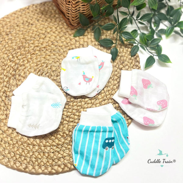 Baby mittens with cartoon designs on a woven mat with a plant in the background.