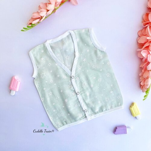 Light green baby vest with white buttons on a light purple background with decorative elements.