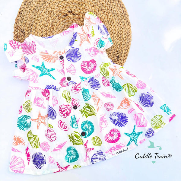 Colorful shell patterned baby bib on a light blue background with a straw hat.