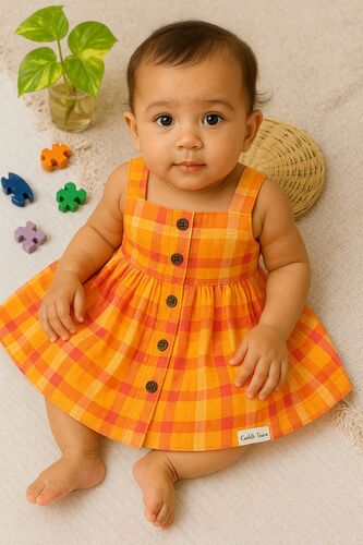 Baby wearing an orange checkered dress sitting on a beige surface with colorful puzzle pieces and a plant.
