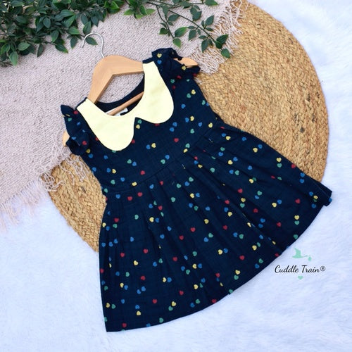 Navy dress with colorful hearts and yellow collar on a hanger against a textured surface.